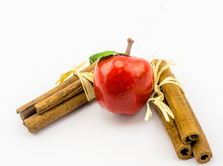 Red wooden apple between cinnamon sticks, isolated in front of white background, decoration for the Christmas tree