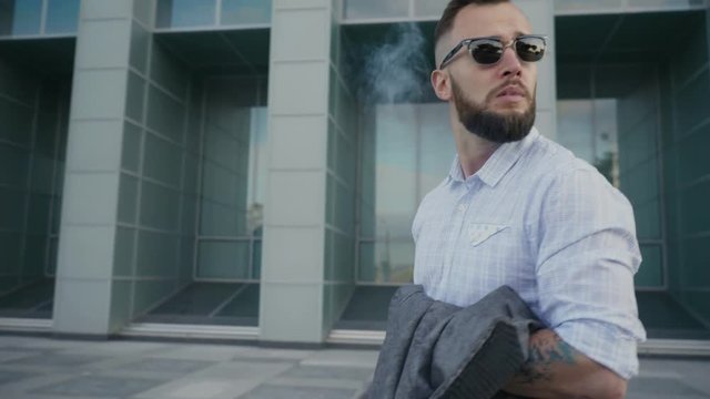 Confident well-dressed man with beard vaping an electronic cigarette
