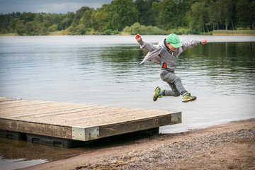 Naklejka premium Young playful caucasian boy running in mid-air making a jump from a jetty to the beach.