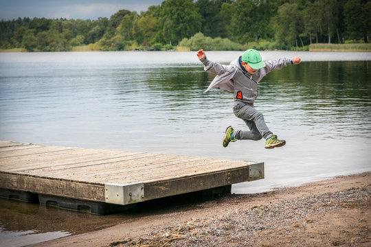 Young playful caucasian boy running in mid-air making a jump from a jetty to the beach.