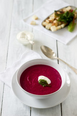 Beet cream soup with sour cream and croutons and a white plate. Rustic style, selective focus.