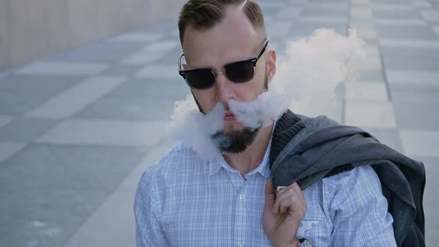 Confident well-dressed man with beard vaping an electronic cigarette