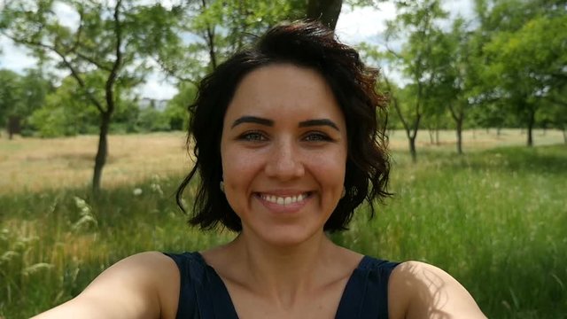 A beautiful brunette woman smiles romantically and turns left and right while keeping somebody`s hands on a sunny day in summer in slow motion