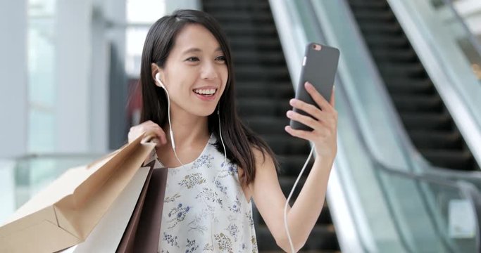 Woman making video call with cellphone and holding shopping bags