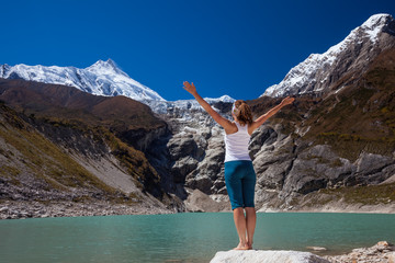 Woman is doing yoga excercises near big lake on the Manaslu circuit trak in Nepala