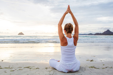 Caucasian woman practicing yoga at seashore of tropic ocean