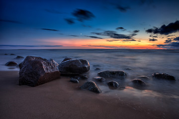 Baltic Sea sunset seascape with wet rocks. Smooth long exposure of waves