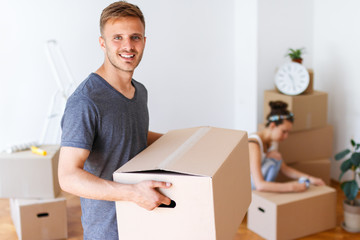 Moving day. Young man carrying cardboard box and smiling.  