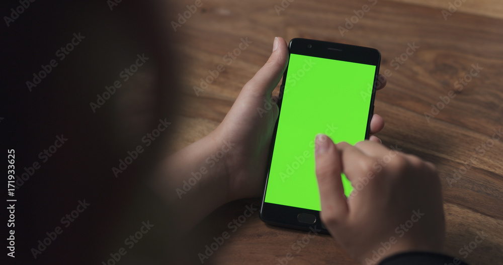 Wall mural female teen girl using smartphone with green screen over wood table