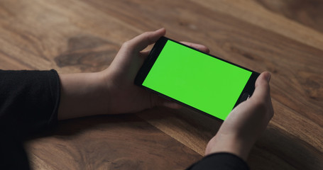 female teen girl hold smartphone with green screen over wood table