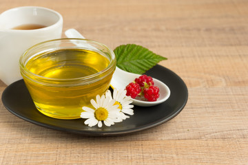 A Cup of honey on the plate. The honey in the spoon drops, raspberry, chamomile, derevyanny background.