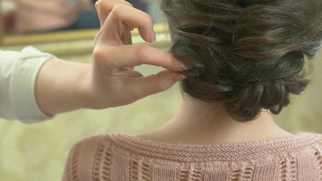 Hand of stylist, braided hairdo. Brown haired woman back view.
