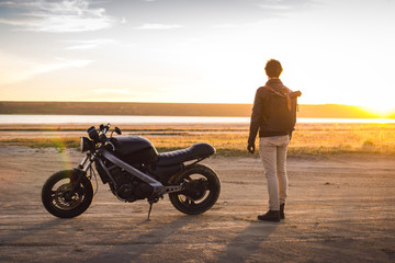 Motorcyclist with his motorbike on the road during sunset