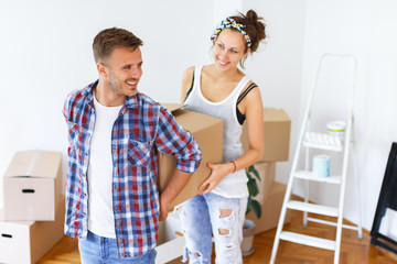 Moving into new apartment. Couple carrying cardboard boxes together.