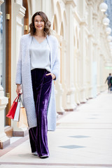 miling beautiful middle aged woman in knitted bright summer coat with shopping bags