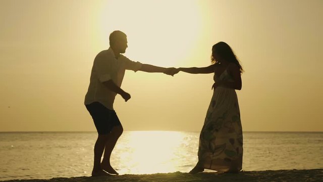 Funny young married couple dancing on the beach. Silhouettes at sunset