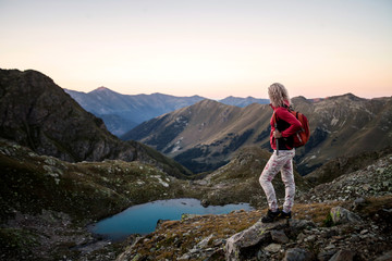 Fototapeta premium Girl hiker standing on a brink rock and looking at the mountains