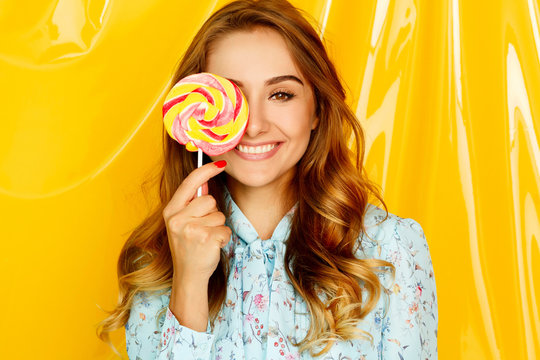 Portrait of a happy pretty student girl holding sweet candy over yellow background