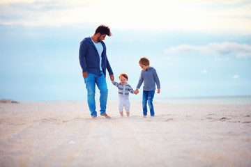 happy father and sons walking on sandy autumn beach near the sea