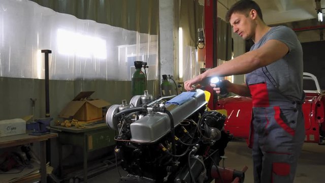 Mechanic working on classic car engine in restoration workshop