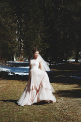 Spring portrait of a bride, dressed in pink wedding dress in the snowy forest.