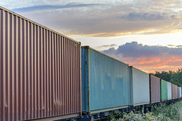 Obraz premium Multicolored railway containers go to the horizon by rail to a beautiful sunset