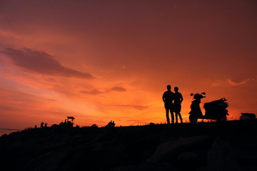 Fototapeta na wymiar couples having sunset at beachside a scooter near to them