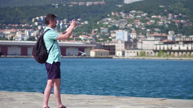 Young handsome bearded man making outdoor photos on the Trieste sea pier
