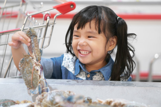 Asian Children Cute Or Kid Girl Holding And Choose Fresh Horse Crab In Ice Tray And Fun With Smile White Teeth For Seafood Sales Or Buy And Shopping With Supermarket Cart At Supermarket Store