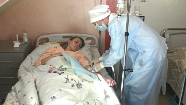 Skillful general practitioner is putting dropper in hospital. Young woman doctor anesthesiologist puts the dropper in hospital room, nurse puts the patient medical drip into a vein