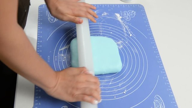 Chef rolling blue fondant with rolling pin