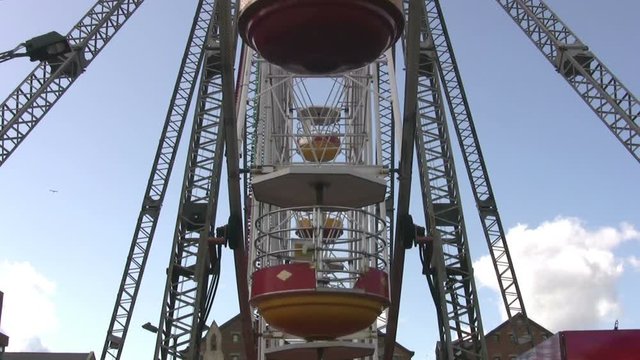Small to medium sized Ferris wheel with cylindical shaped capsules, viewed end on in an urban setting. The ride of the type which can be easily dismantled, used in travelling fairs. Lockdown shot.