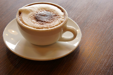 fresh hot cappuccino coffee in white cup on wood table in the morning for breakfast drink before work on warm white and nature light at cafe restaurant or office with space