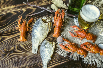 Dried salted fish with boiled red crayfish, glass with beer and a bottle of beer on canvas lying on dark wooden boards
