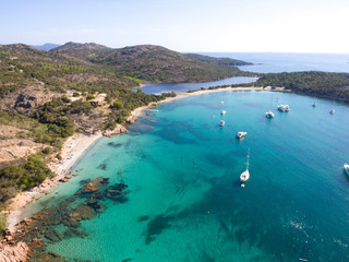Aerial drone view of Rondinara Bay with sailing boats and people swimming at the sunny beach