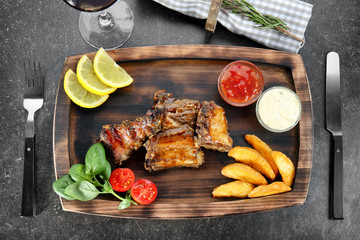 Wooden tray with delicious ribs and vegetables on table