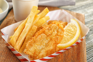 Paper box with tasty fried fish and potato chips on table, closeup
