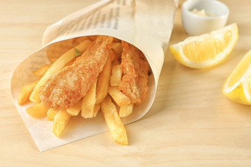 Tasty fried fish and potato chips rolled in paper on wooden table
