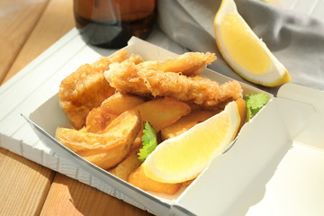 Paper box with tasty fried fish and chips on table