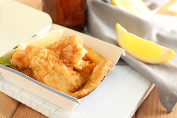 Paper box with tasty fried fish and chips on table