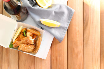 Paper box with tasty fried fish and chips on table