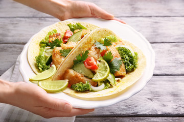 Woman holding plate with tasty fish tacos over wooden table