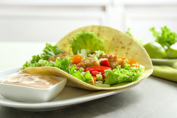 Plate with tasty fish taco and sauce on table