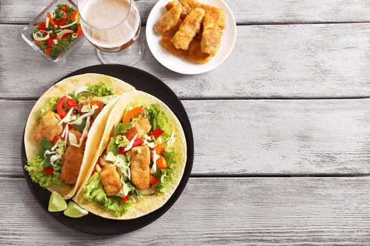 Plate with tasty fish tacos on wooden table