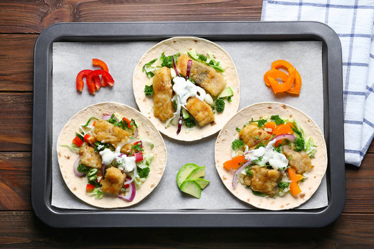 Baking tray with tasty fish tacos on wooden table