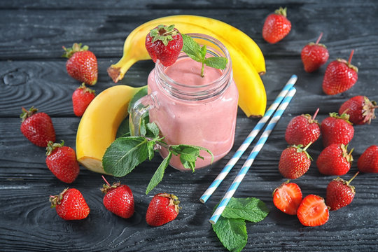 Mason jar with fresh strawberry and banana smoothie on wooden table