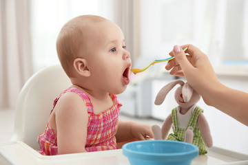 Mother feeding baby with spoon indoors