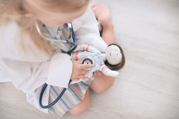Little girl in medical coat playing with doll on floor