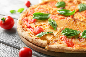 Delicious pizza with tomatoes and fresh basil on kitchen table