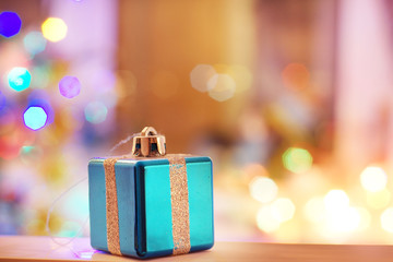 New Year card with toy in the form of a gift with a ribbon on a background of blurred lights of the Christmas tree